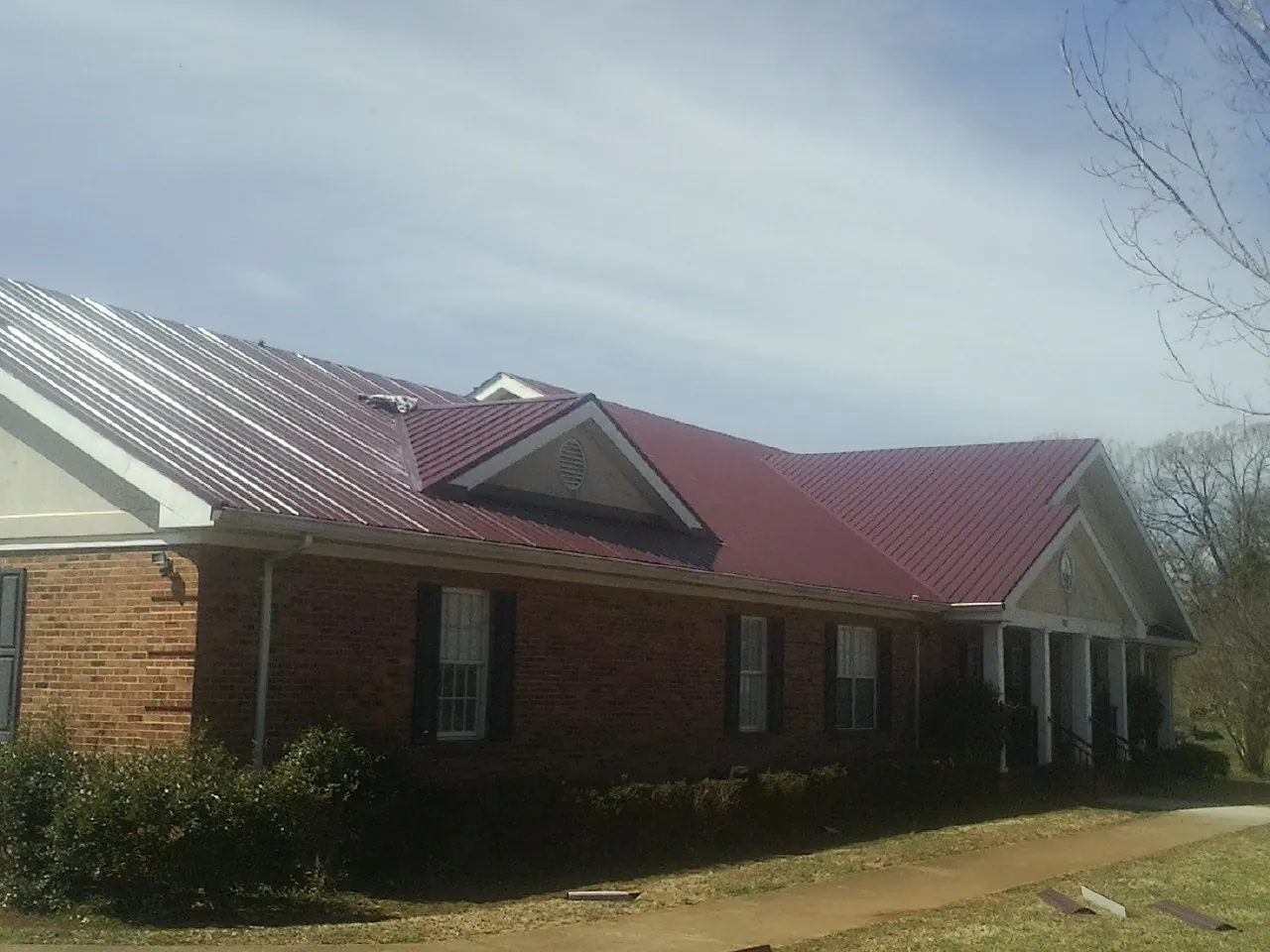 Red metal roof with gabled entries on a long brick building, from a Hail Damage Roof Repair job in Ashuelot