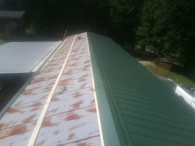 Old rusted panels beside newly installed green metal roofing — Wind Damage Roof Repair by Roofing Brothers in Ashuelot