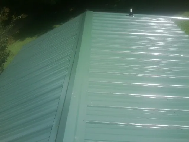 New green metal panels meeting at the ridge of a roof — Flat Roof Repair work by our crew in Ashuelot