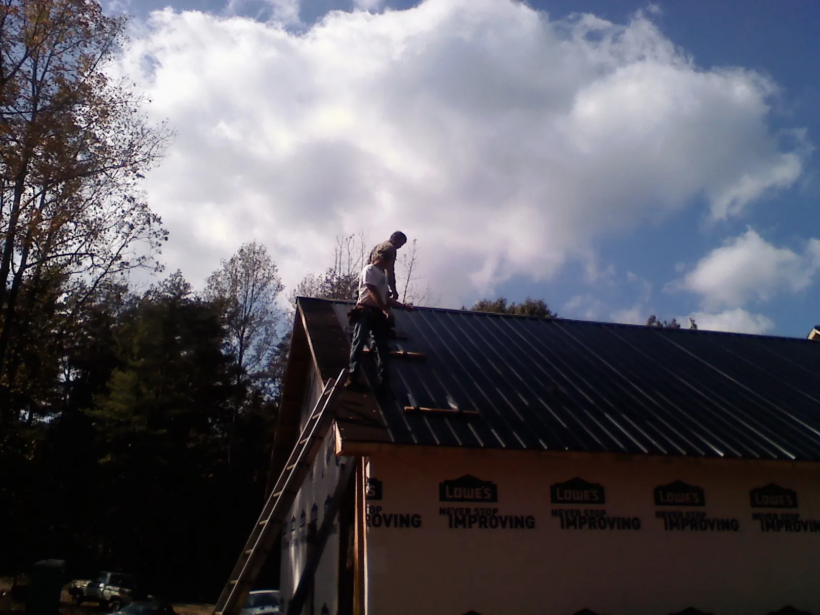 Roofer fastening dark metal panels high against a cloudy sky, from a Roof Inspection job in Ashuelot