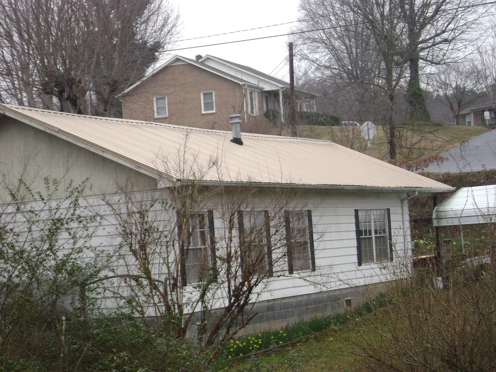 Tan metal roof on a white sided house set into a hillside — Commercial Roofing by Roofing Brothers in Ashuelot