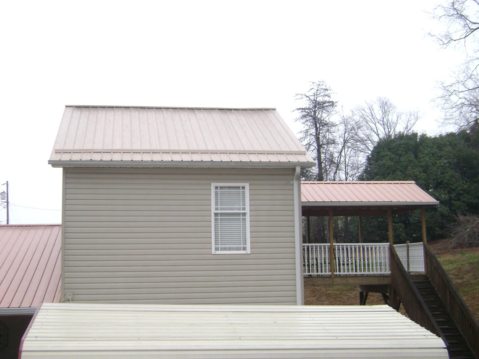 Tan metal roofs on a two story addition and attached porch, from a Roof Replacement job in Ashuelot